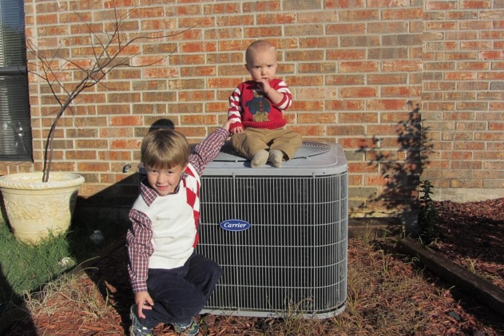 two kids sitting on and near ac unit
